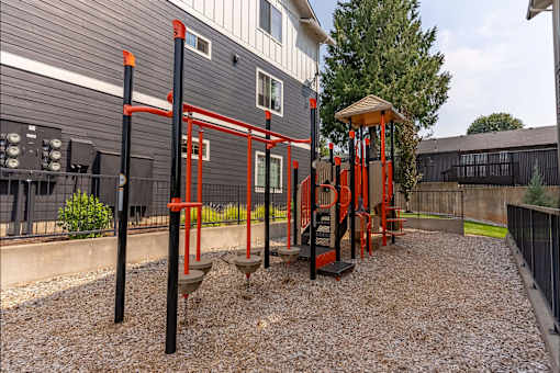 A playground with a red swing set and a black fence at Sandyplace Apartment Homes, Sandy, OR, 97055