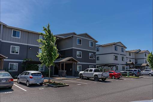 A parking lot with cars and apartment buildings in the background at St Helens Place Apartment Homes, St Helens, Oregon