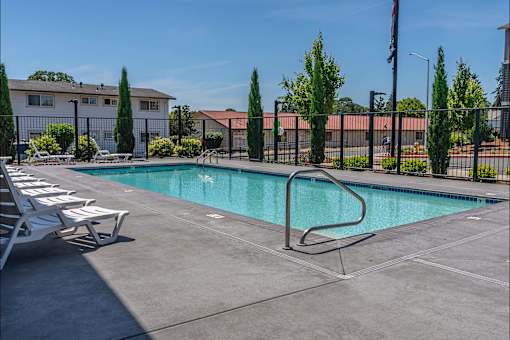 A pool surrounded by a fence and trees with chairs around it at St Helens Place Apartment Homes, Oregon