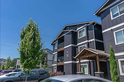 A grey building with a tree in front of it. at St Helens Place Apartment Homes, St Helens, OR