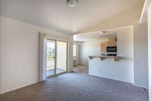 A spacious living room with a grey carpet and a sliding glass door leading to a balcony at Stoneplace Apartment Homes, Molalla, OR, 97038