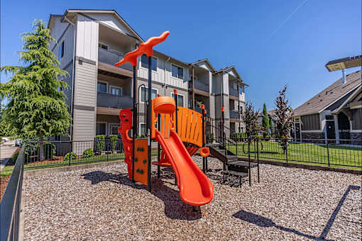 A playground with a slide and a climbing frame in front of a residential building at Timberridge Place Apartment Homes, Albany, OR