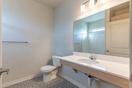 A bathroom with a toilet, sink, and mirror at Woodburn Place Apartment Homes, Woodburn, 97071