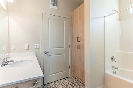 A bathroom with a sink, a door, and a bathtub at Woodburn Place Apartment Homes, Woodburn, Oregon