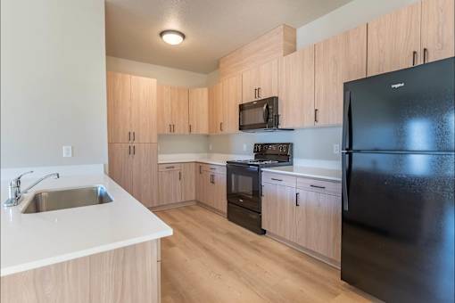 A kitchen with wooden cabinets and a black refrigerator at Woodburn Place Apartment Homes, Woodburn, OR