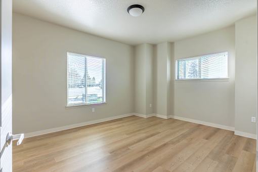 A room with wooden flooring and two windows at Woodburn Place Apartment Homes, Woodburn, OR
