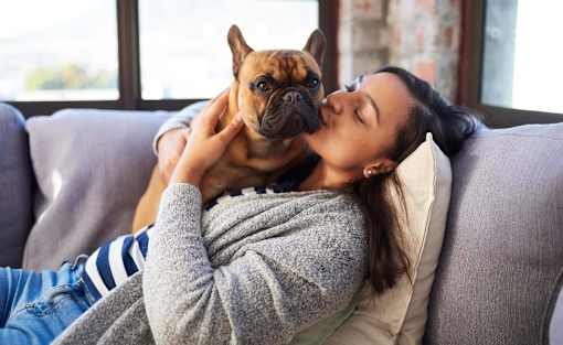 A woman is cuddling with a dog on a grey couch at The Hub Hermiston Apartments, Hermiston, Oregon