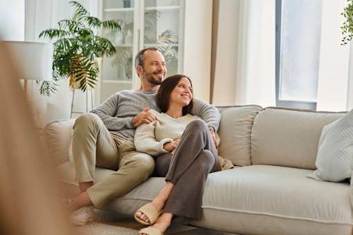 A man and woman are sitting on a couch, holding hands and smiling at each other at The Hub Hermiston Apartments, Hermiston