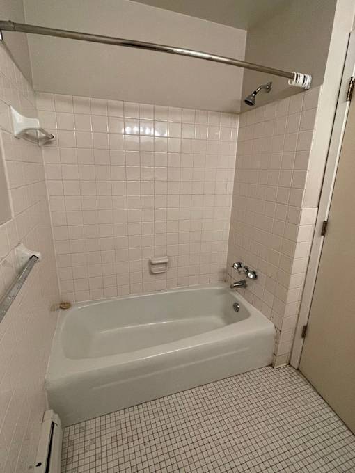 A white tiled bathroom with a white tub and a white door.