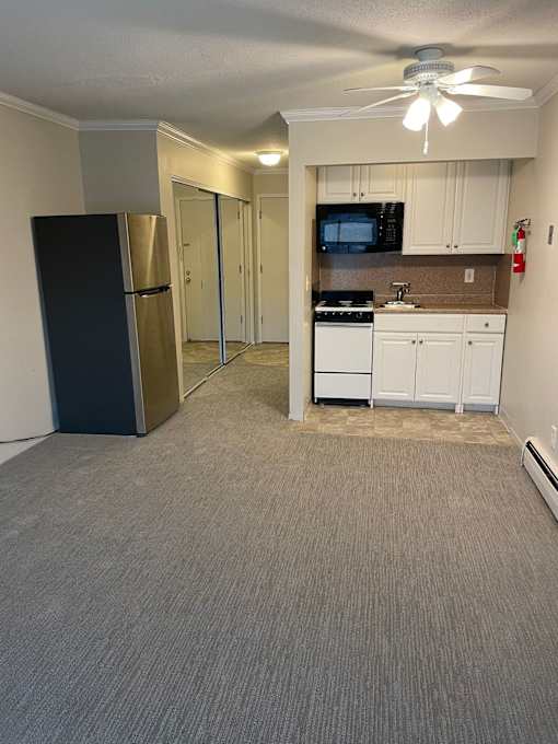 A black refrigerator is in a kitchen with white cabinets and a microwave.