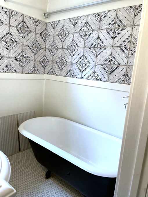 A black and white bathtub in a bathroom with a grey and white tiled wall.