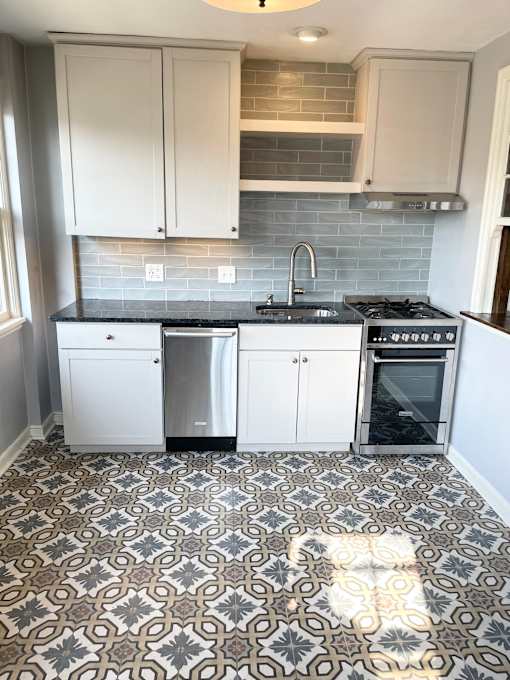 Designer kitchen with decorative floor tile, custom cabinetry, granite countertops, tiled backsplash and stainless steel appliances, including dishwasher.