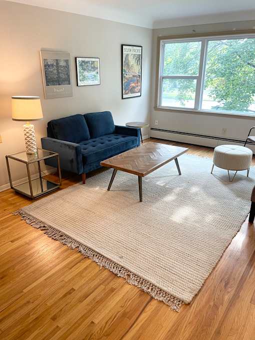 A living room with a blue couch, a table, and a rug.