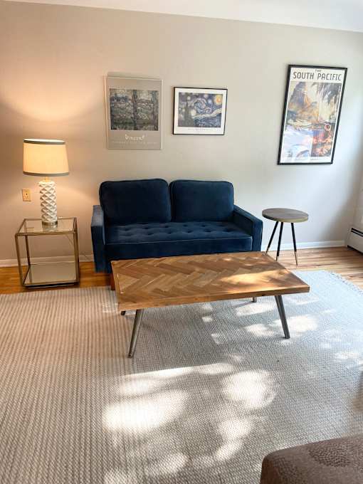 A blue couch sits in a living room with a lamp and a painting on the wall.