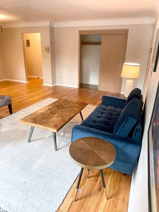 A living room with a blue couch, a wooden coffee table, and a white rug.