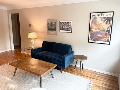 A living room with a blue couch, a wooden coffee table, and a poster on the wall.
