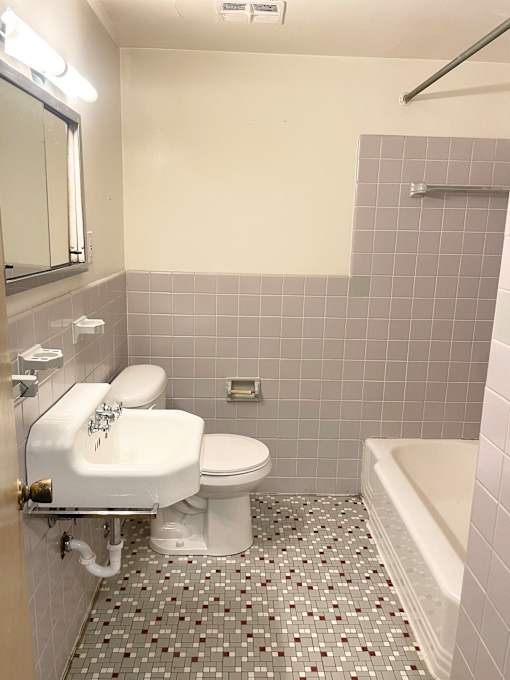 A white toilet with a sink is in a bathroom with grey tiles.