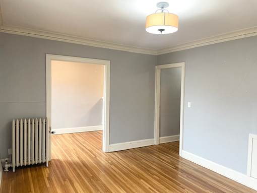 A room with a white wall and a wooden floor with a radiator.