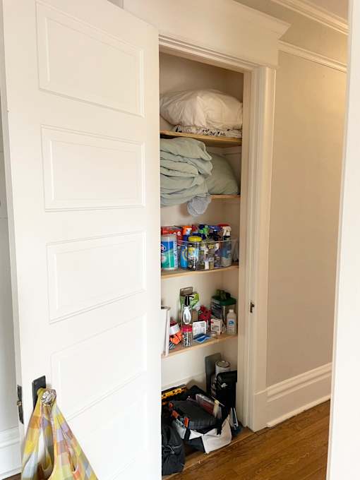 A white door is open to a small closet with a shelf and some items on it.