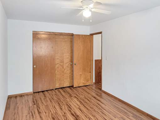 A room with a ceiling fan and a wooden floor with two doors.