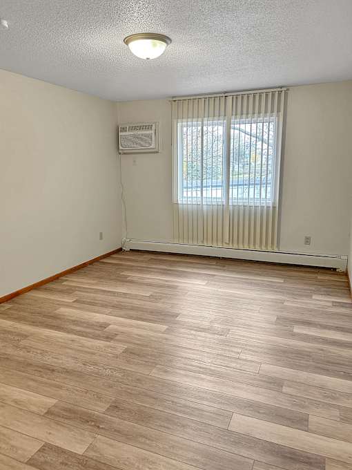 A room with a window covered by blinds and a wall-mounted air conditioner unit.
