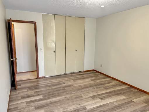 A room with a wooden floor and a white wall with a door and a wardrobe.