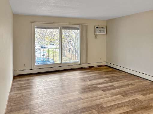 A room with wooden flooring and a window overlooking a parking lot.