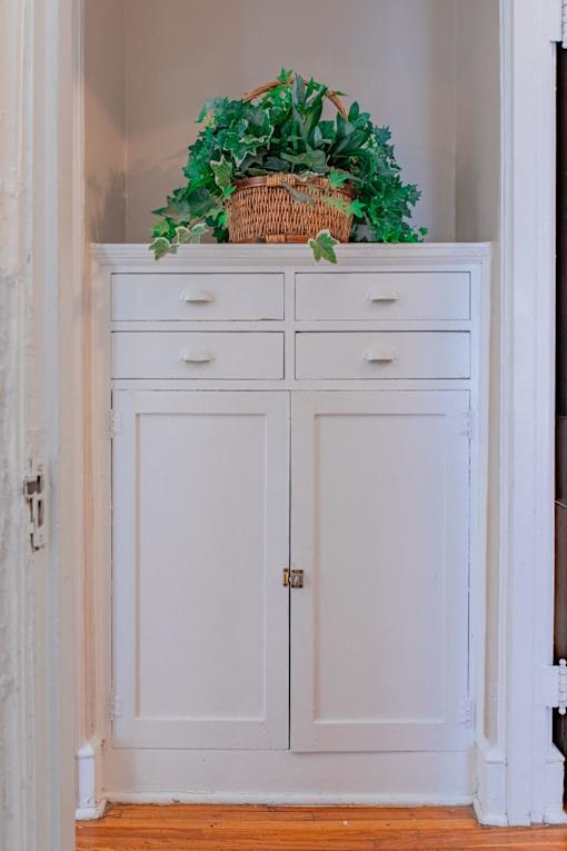 A white cabinet with a basket of green plants on top.