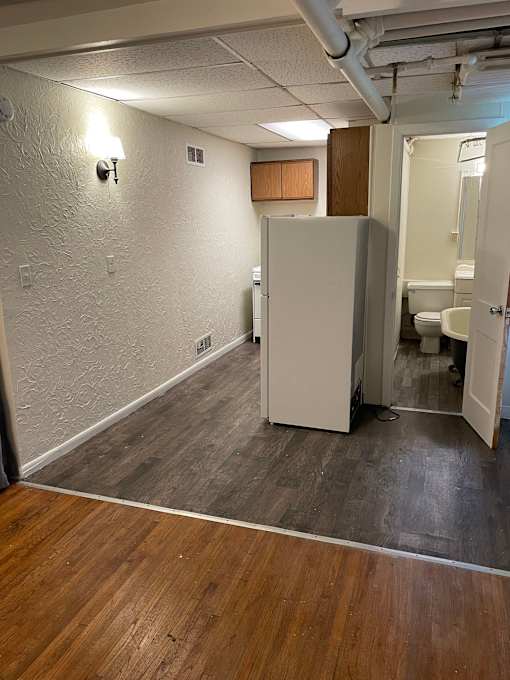 A white refrigerator in a room with wooden floors and a white wall.