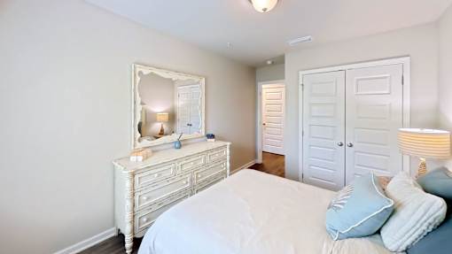 A white bedroom with a bed, dresser, and mirror.