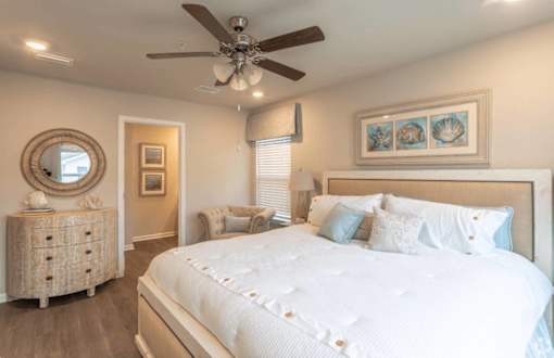 A bedroom with a large bed, a dresser, and a ceiling fan.