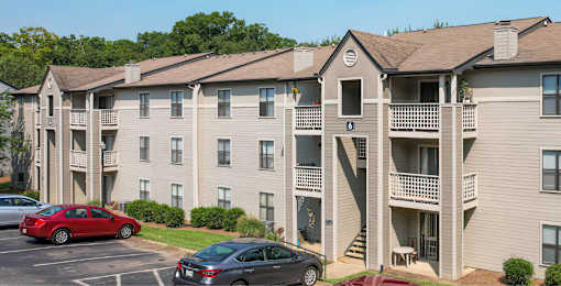 A red car is parked in a parking lot in front of a building.