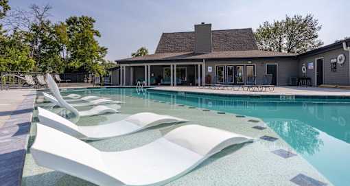 A pool with a white lounger in the foreground and a house in the background.