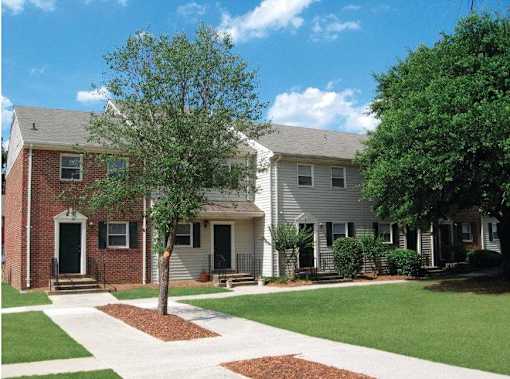 A tree in front of a house with a red brick wall.