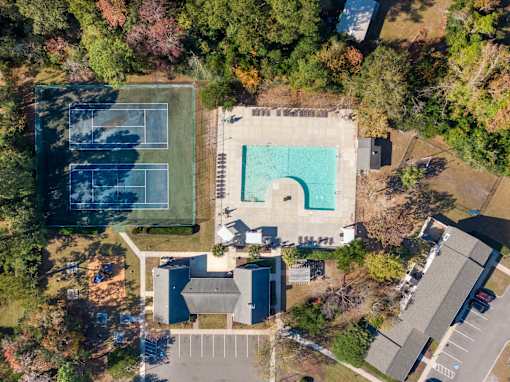 An aerial view of a tennis court and a swimming pool surrounded by trees and buildings.