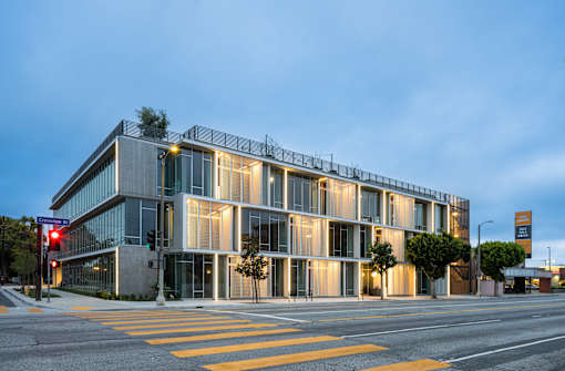 A modern building with a glass facade is illuminated from within and surrounded by a yellow crosswalk.