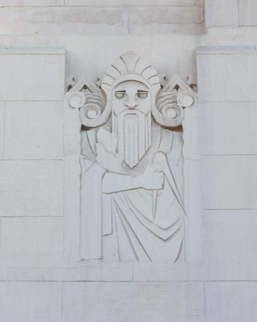 A white stone carving of a man with a beard and a crown on his head.