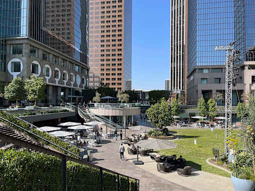 A city park with people walking around and tall buildings in the background.