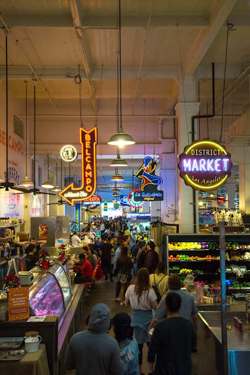 A busy market with a neon sign that says District Market.
