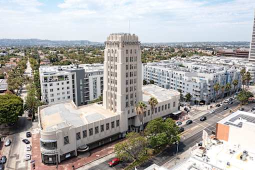 A tall white building with a sign on the top is in the middle of a city street.