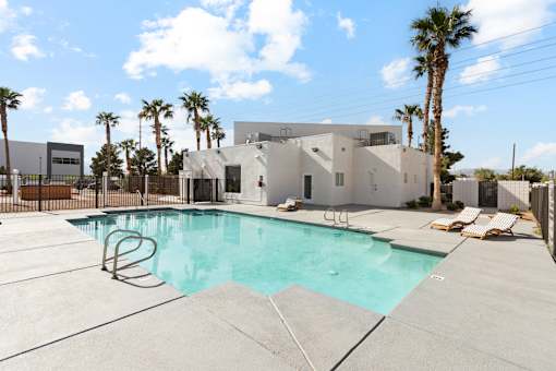 A swimming pool in front of a house with a fence and palm trees.