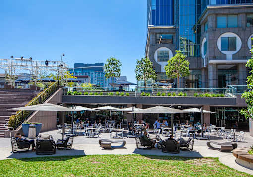A large outdoor seating area with people dining and a modern building in the background.