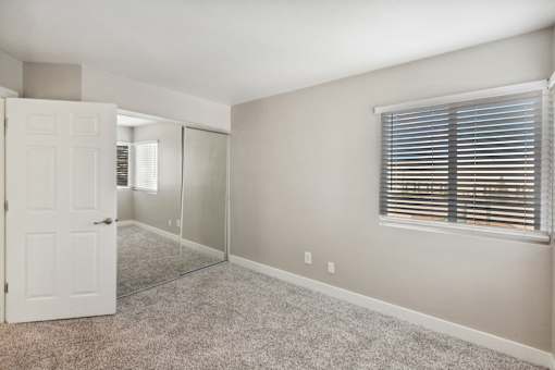 A room with a white door, carpeted floor, and a window with blinds.