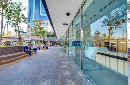 A glass-walled building with people sitting on benches outside.