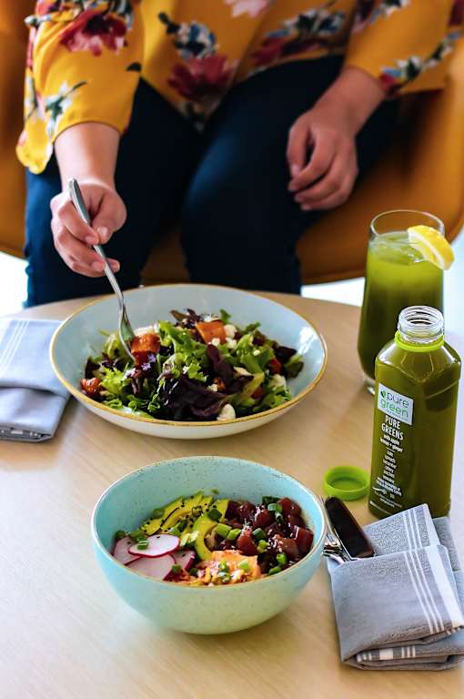 A person is eating a salad with a lemon wedge and a bottle of green juice on the table.