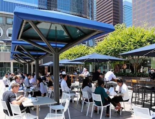 People are sitting at tables under blue umbrellas in an outdoor dining area.