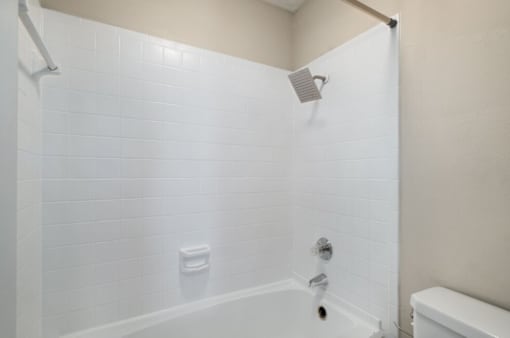 A white tiled shower with a white tub and a white shower head.