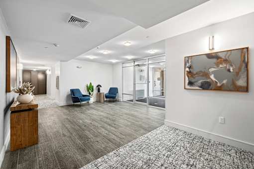 A spacious hallway with a large painting on the wall and two blue chairs.