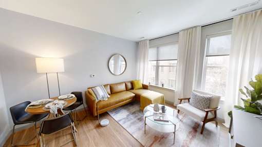 A living room with a brown couch, a coffee table, and a round mirror on the wall.
