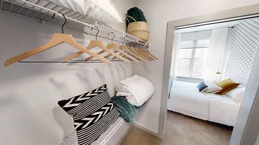 A white bedroom with a bed, pillow, and clothes hanging on a rack.